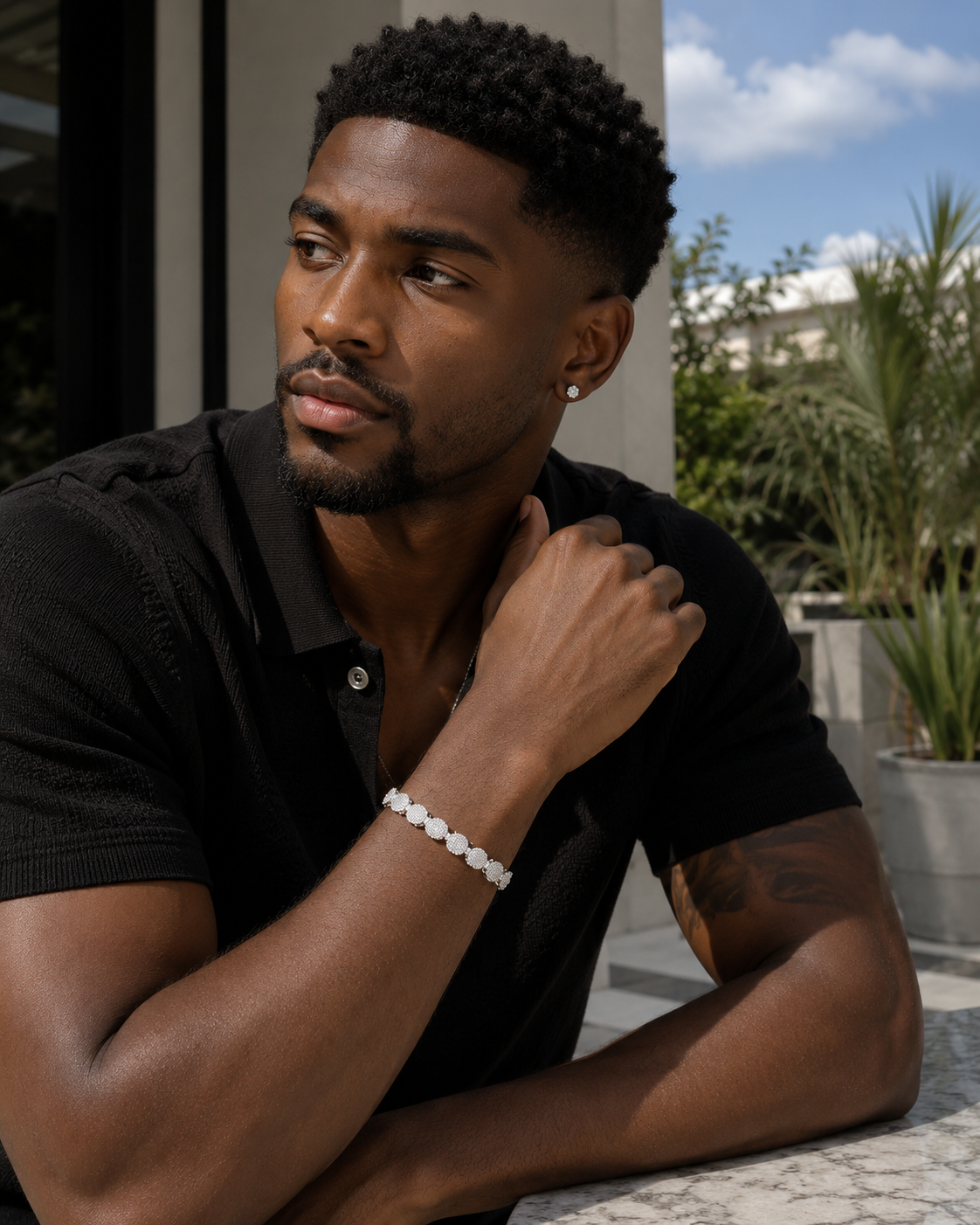 Man wearing a black shirt with a bracelet, sitting outdoors.