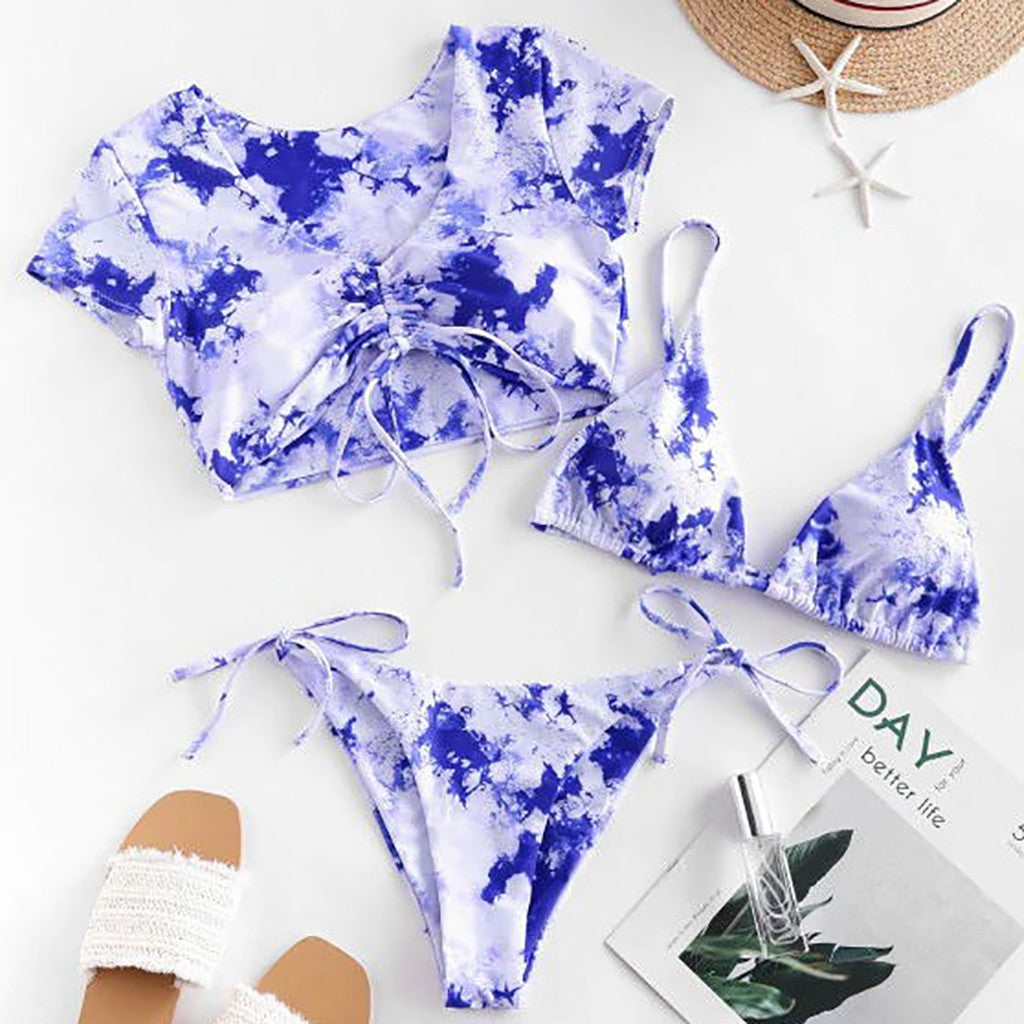Blue and white  bikini set on a white surface with a hat, magazine, and sandals.