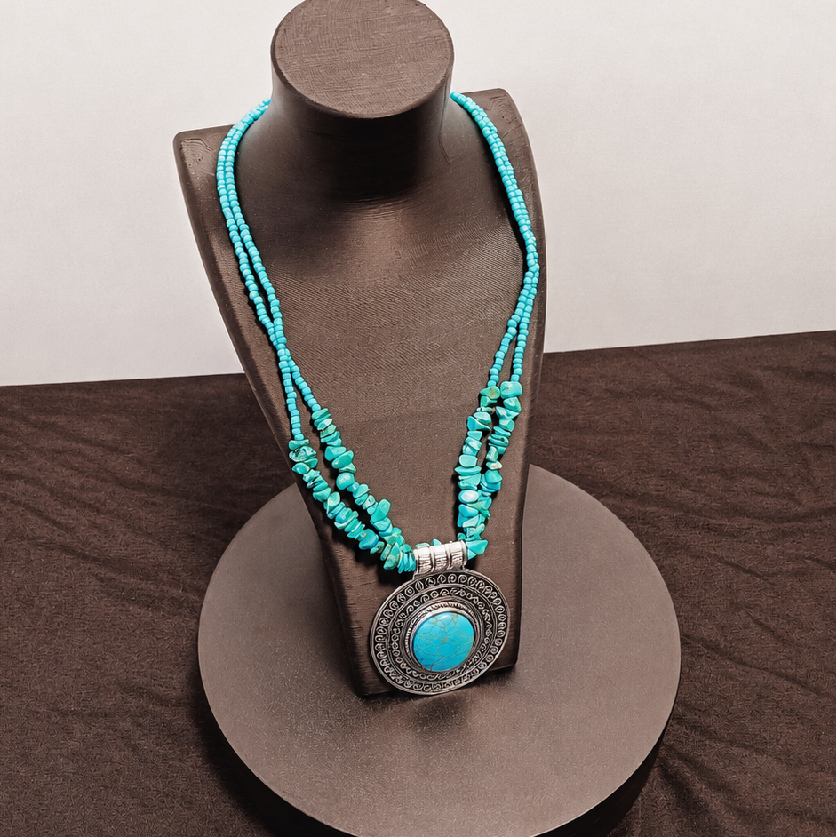 Turquoise beaded necklace with a large pendant on a brown stand against a brown background