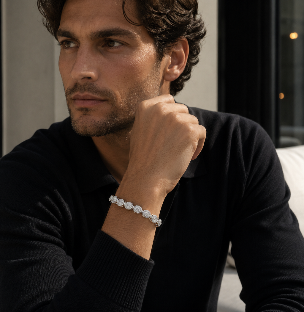Man wearing a black sweater and bracelet, sitting indoors.