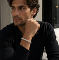 Man wearing a black sweater and bracelet, sitting indoors.