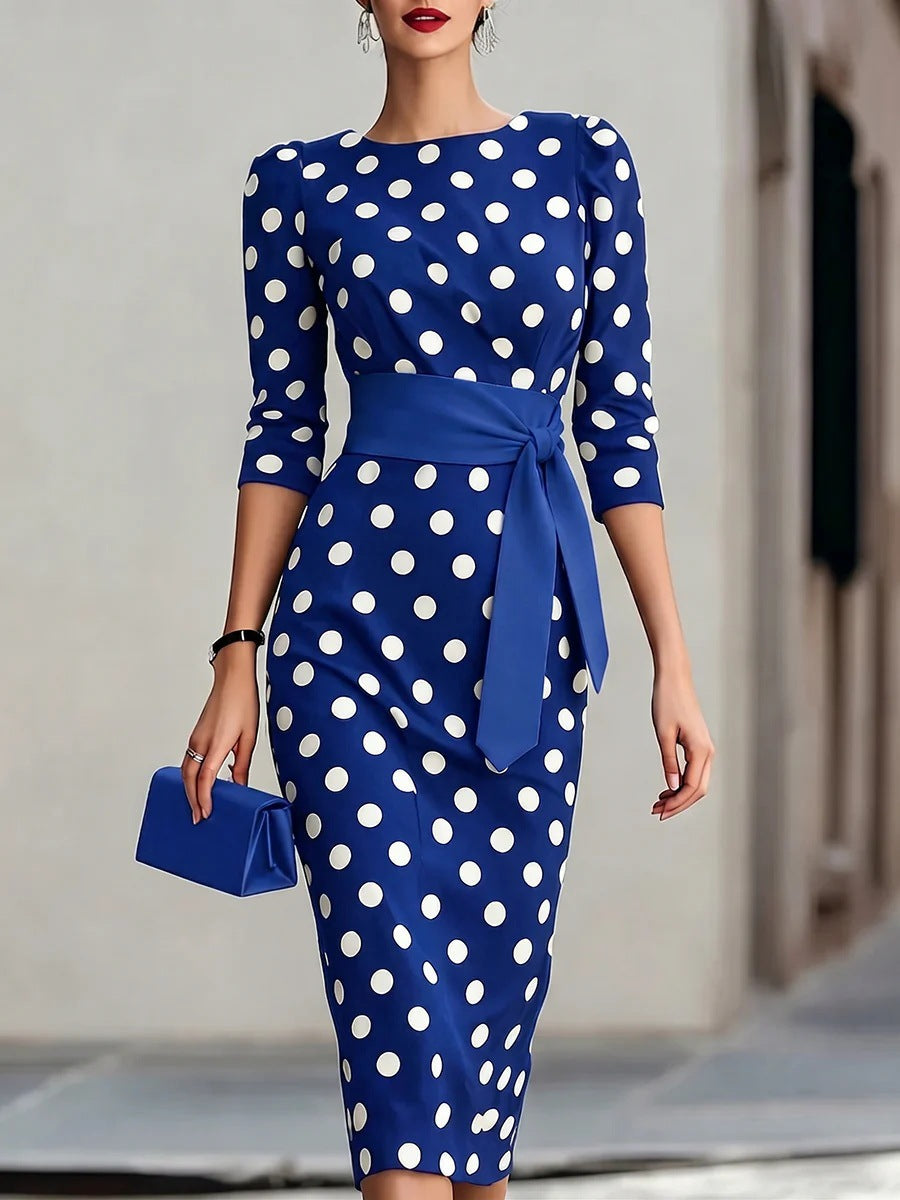Woman wearing a blue dress with white polka dots holding a matching clutch.