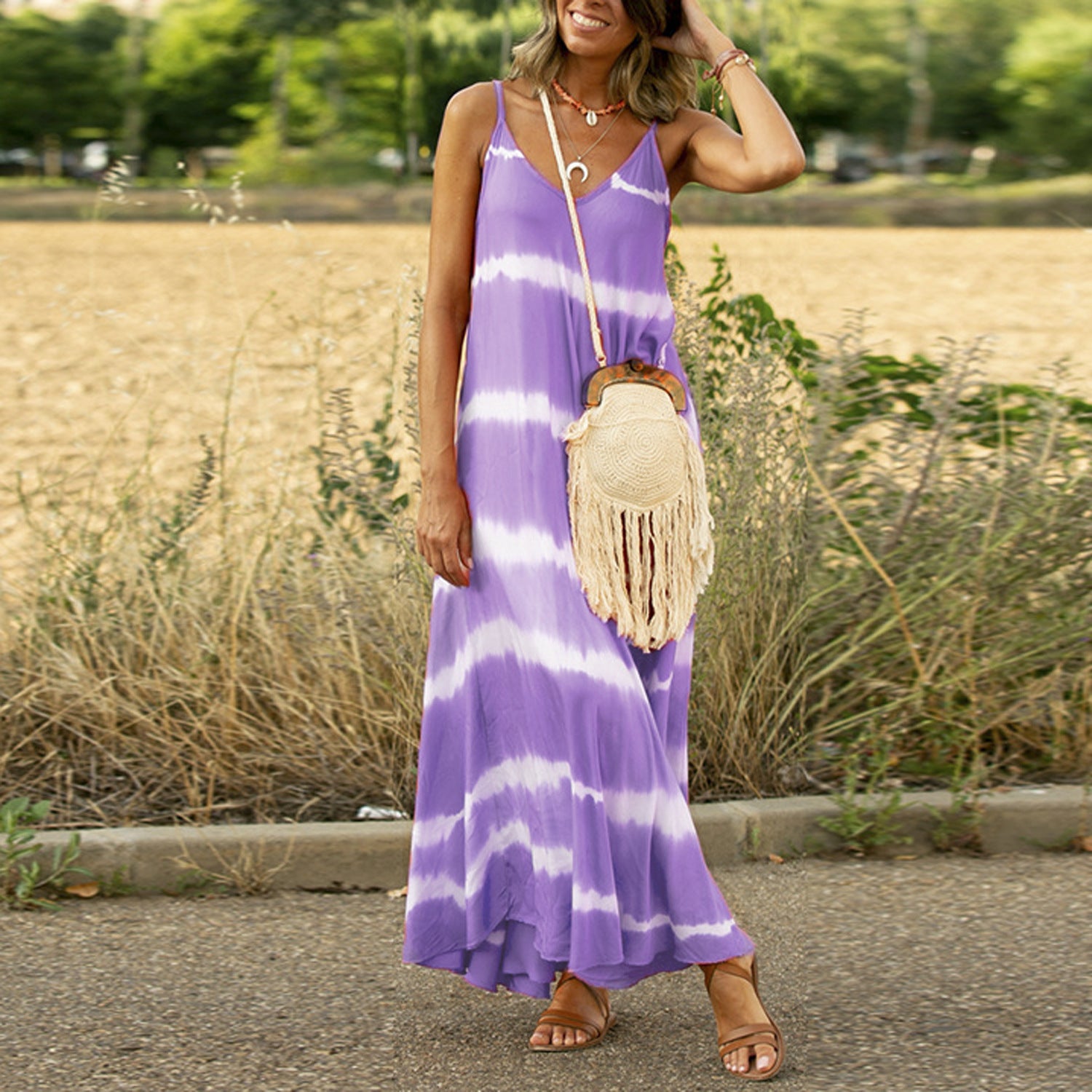 Woman wearing a purple and white striped dress with a straw bag in an outdoor setting.