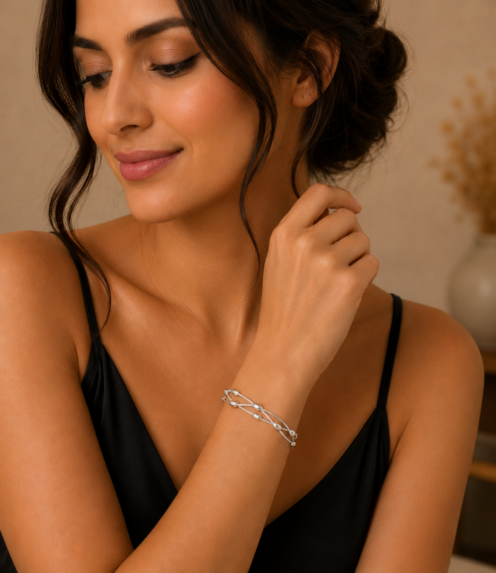 Woman wearing a silver bracelet, looking at her hand with a neutral background