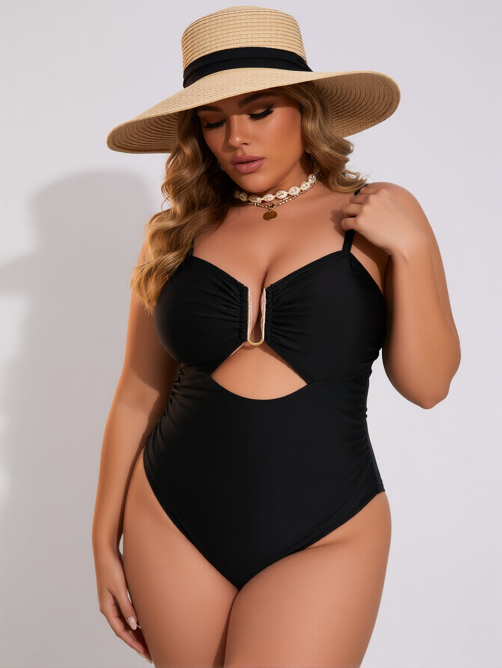 Woman wearing a black swimsuit and wide-brimmed hat on a plain background