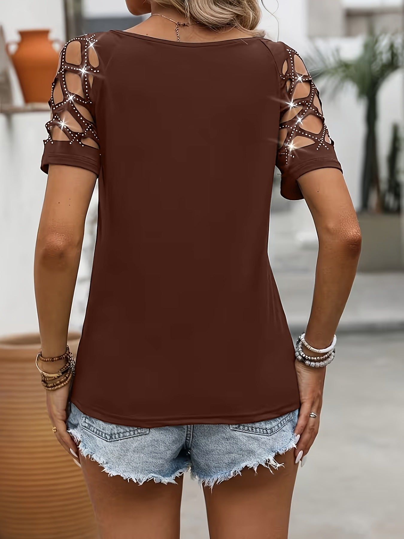 Brown top with cut-out shoulders worn by a person, with a blurred outdoor background.