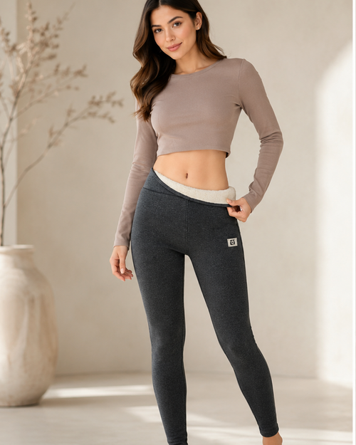 Woman wearing dark gray leggings with a beige top, standing indoors.