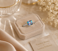Ring with a colorful gemstone on a beige velvet box with decorative text card.