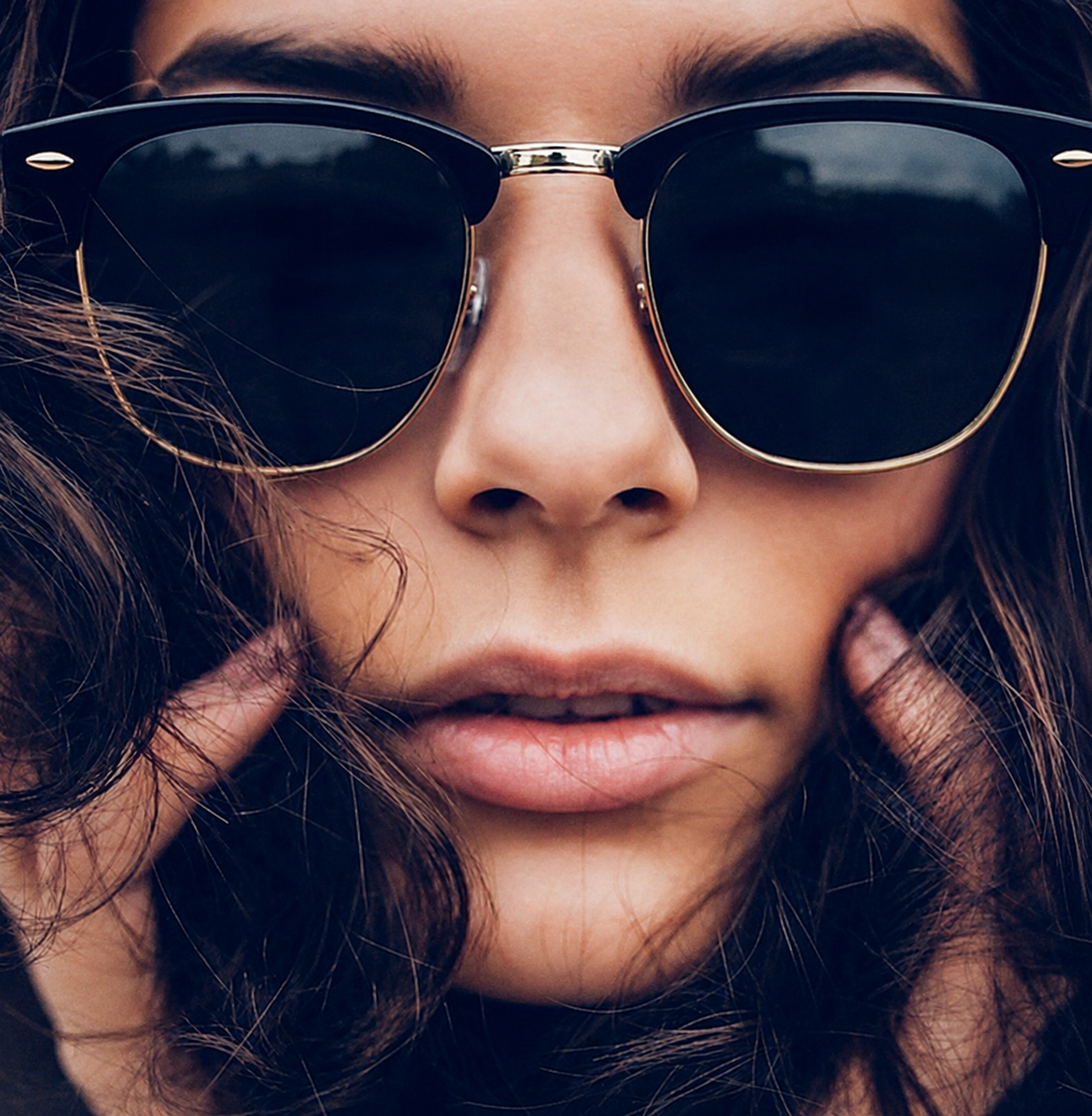 Close-up of a person wearing sunglasses with hands on the sides of their face.