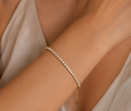 Gold bracelet with small stones on a person's wrist against a neutral background
