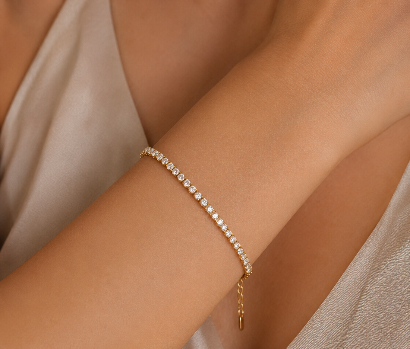 Gold bracelet with small stones on a person's wrist against a neutral background