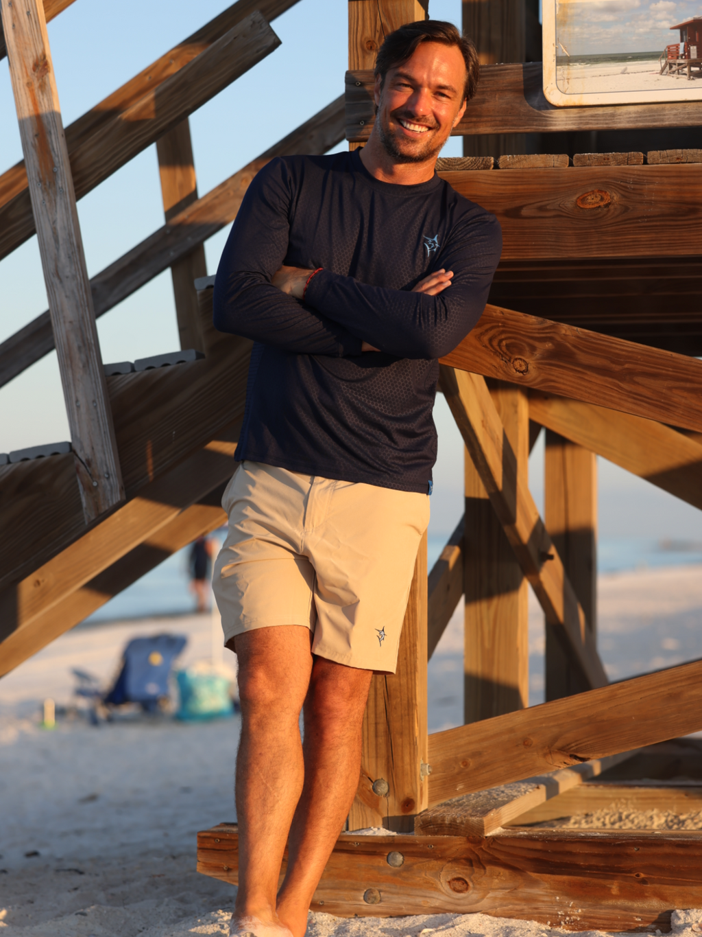 Man standing on a wooden staircase at the beach with arms crossed.