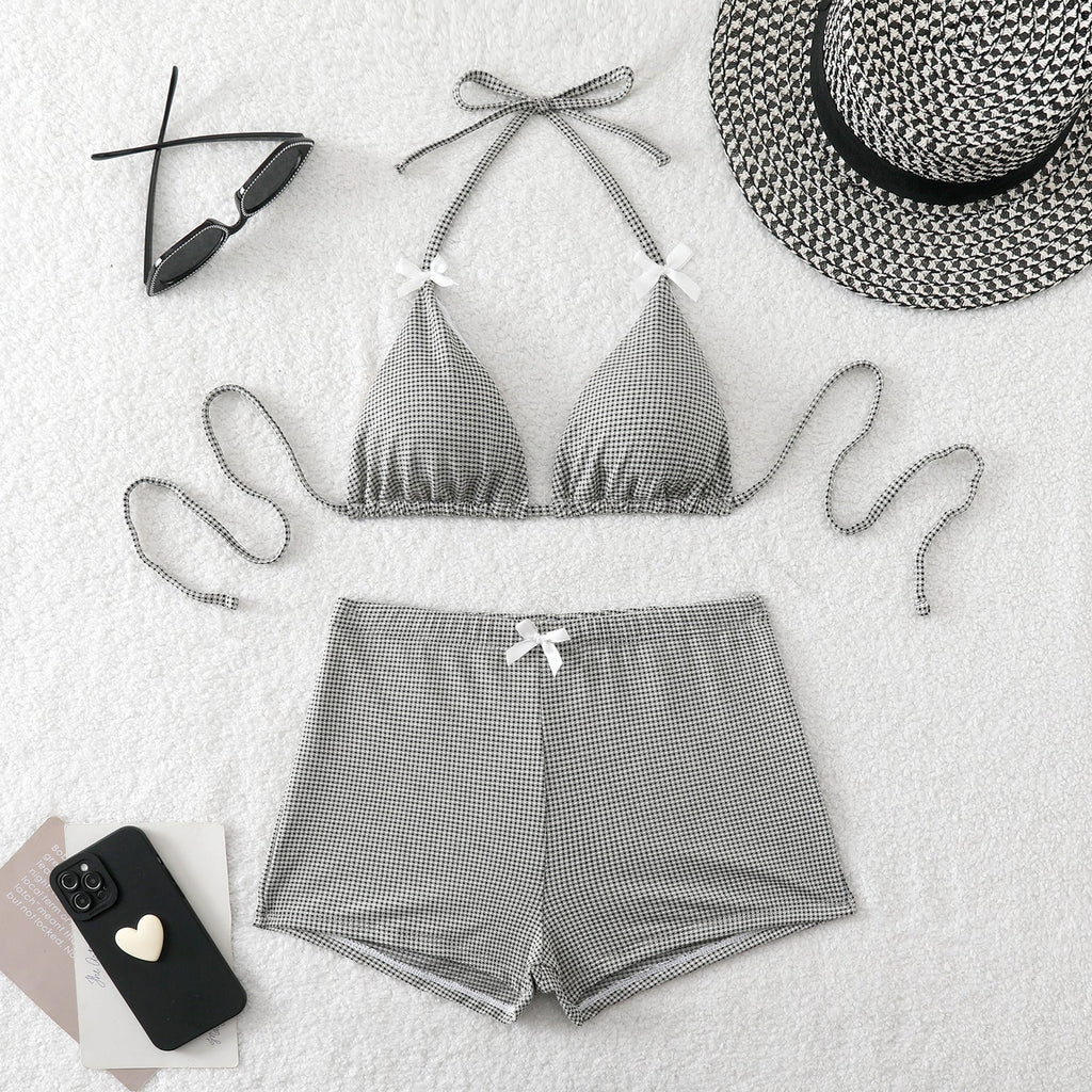 Gray checkered bikini set with matching shorts, sunglasses, and a hat on a light background.
