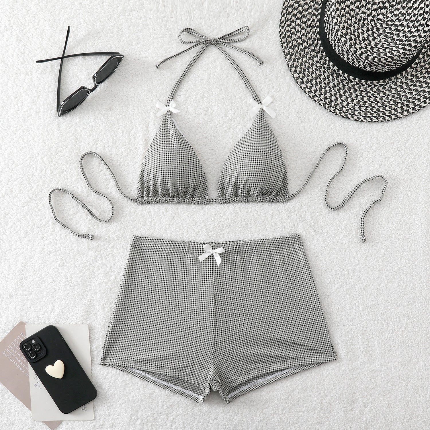 Gray checkered bikini set with matching shorts, sunglasses, and a hat on a light background.