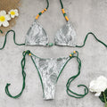 Lace bikini set with green straps on a gray surface with flowers.