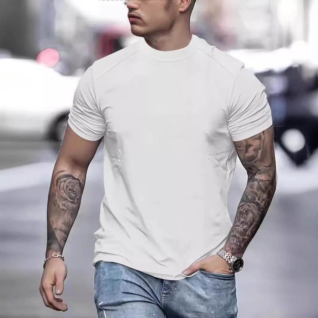 Man wearing a white t-shirt and blue jeans with tattoos on his arms, walking outdoors.