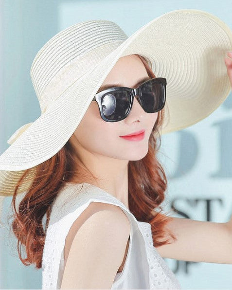 Woman wearing a large beige sun hat and sunglasses with a blurred background