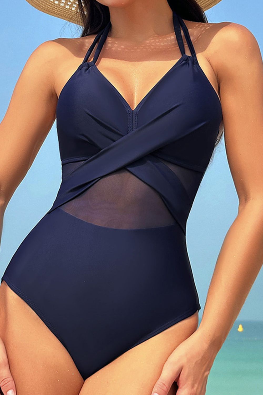 Navy blue swimsuit with mesh panels worn by a person against a beach background