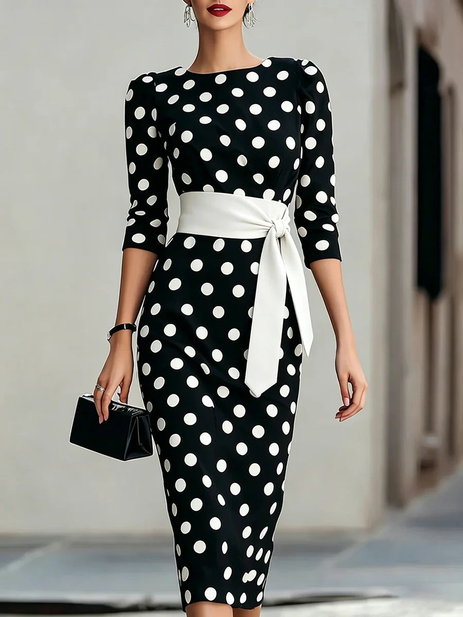 Woman wearing a black dress with white polka dots and a white belt.