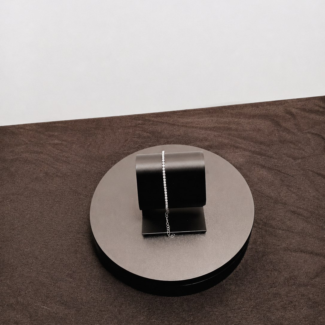 Silver necklace on a round metallic stand with a white background