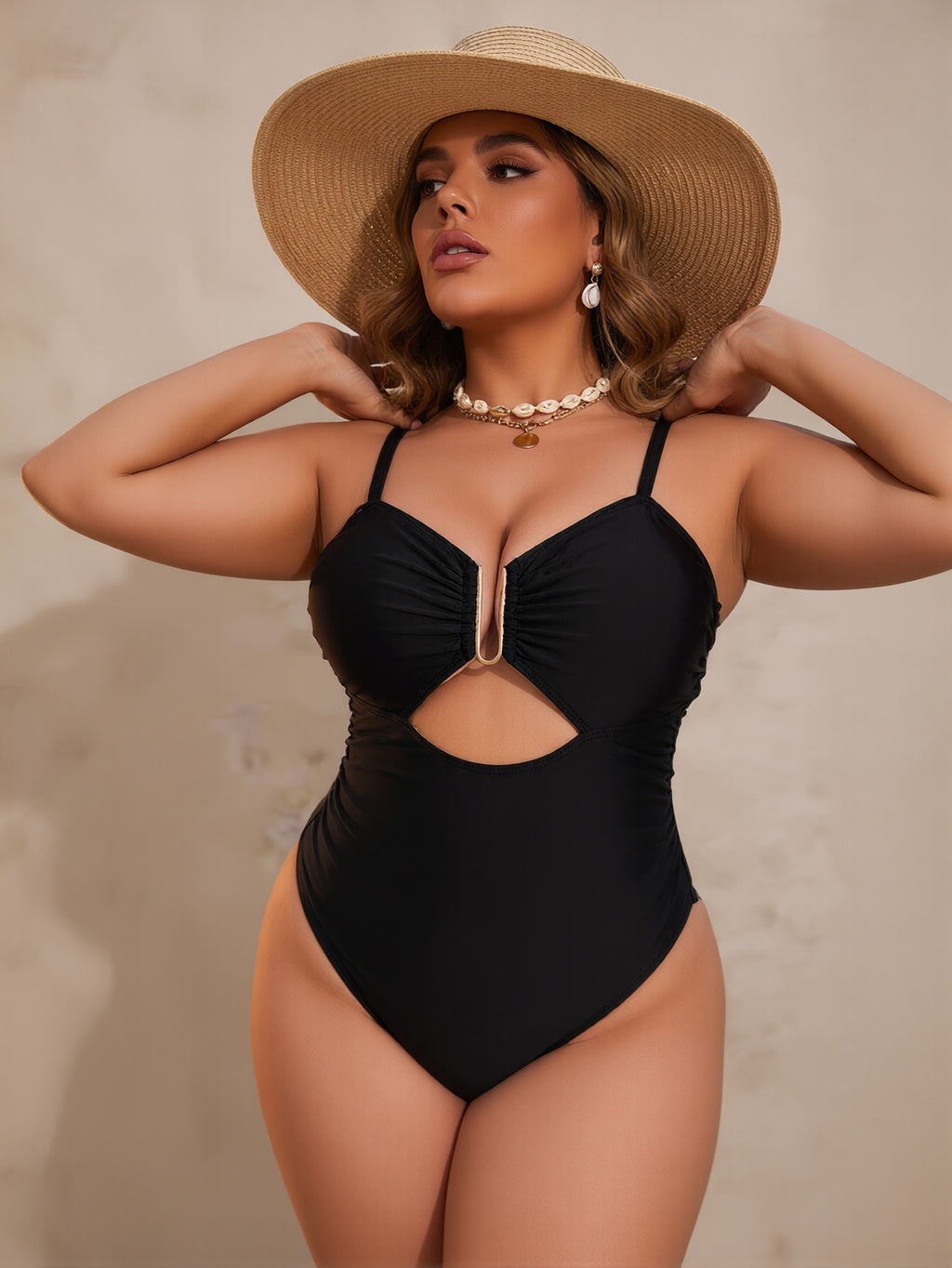 Woman wearing a black swimsuit and straw hat against a neutral background
