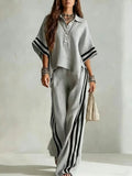 Woman wearing a light gray outfit with black stripes against a plain background