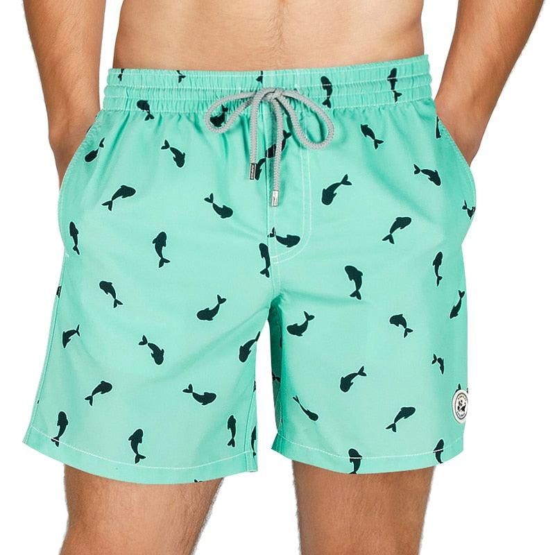 Teal swim shorts with black fish pattern worn by a person on a white background
