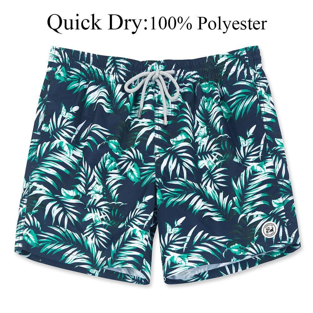 Navy blue swim shorts with green leaf pattern on a white background
